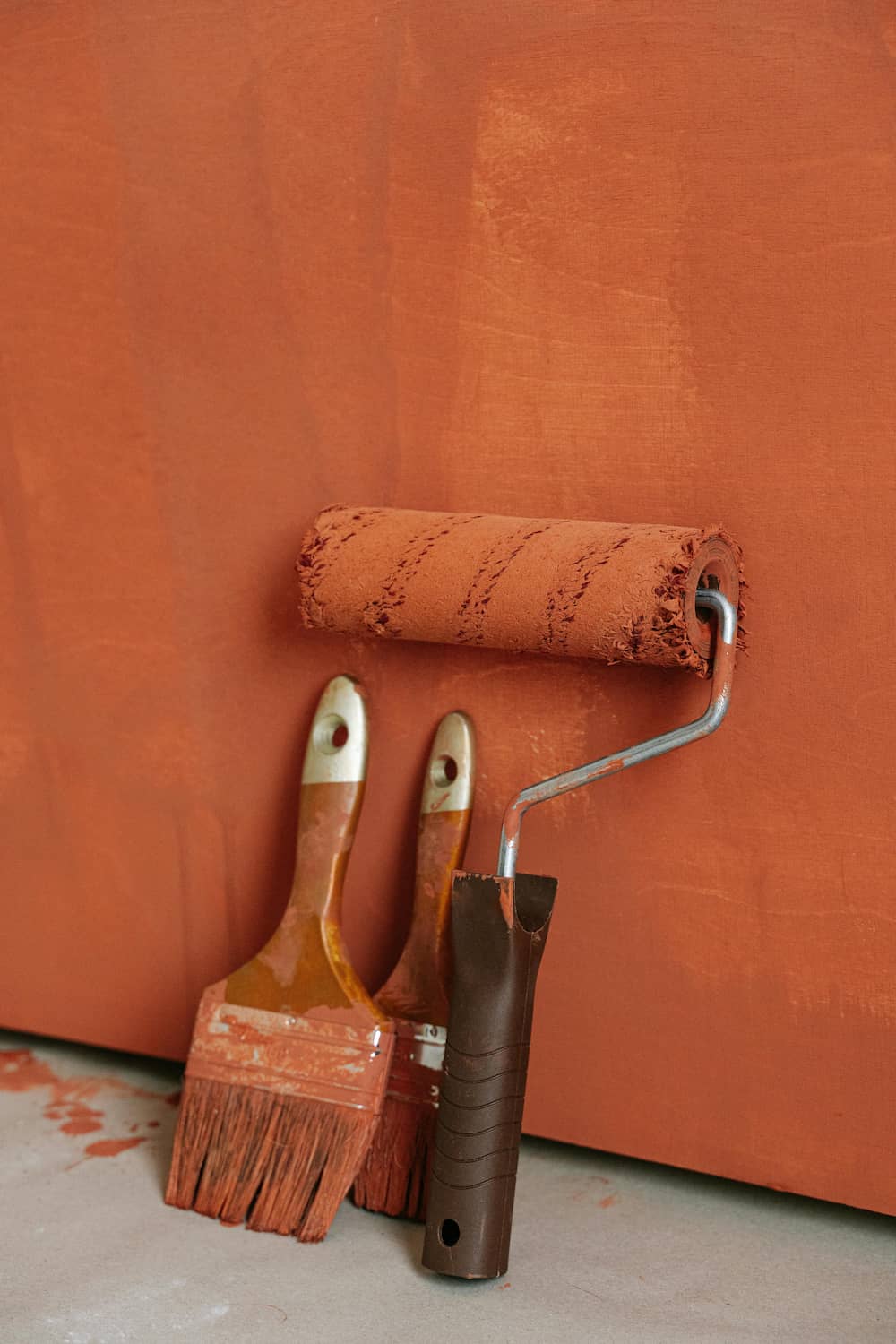 Rulli e pennelli professionali appoggiati a una parete appena tinteggiata color terracotta, simbolo di finiture di alta qualità.
